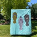 Woollypetals Manatee Migration Quilt displayed on grass with three appliqued manatees