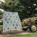 Woollypetals Moonrise quilt displayed against military equipment with green trees