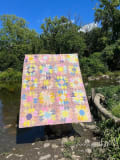Woollypetals Stargeese quilt displayed by a river with colorful star and flying geese blocks