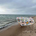 Woollypetals Stargeese quilt held up on a beach with ocean waves