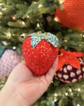 Woollypetals Strawberry Pillow ornament held in hand near decorated Christmas tree