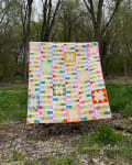 Woollypetals StarBeam Quilt displayed outdoors with colorful patchwork fabrics