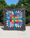 Woollypetals Wash Your Paws quilt with colorful star blocks and teal cross on dark background