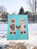 Woollypetals Don't Let Go Quilt featuring two otter figures holding hands on turquoise background