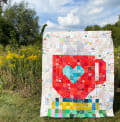 Woollypetals Book Date Patchwork Quilt with red heart center displayed outdoors