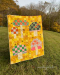 Woollypetals Capped quilt hung outdoors with yellow patchwork background and appliqued house designs