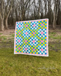 Woollypetals New Star quilt with blue, yellow, and pink blocks displayed outdoors