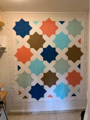 Woollypetals Floored quilt with geometric stars in blue, orange, green, and brown