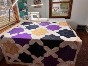 Woollypetals Floored quilt displayed on sewing table with purple, black, and gold star blocks