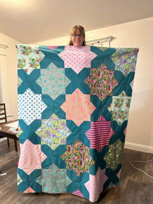 Woollypetals Floored quilt held up by woman showing teal X blocks and colorful medallion blocks