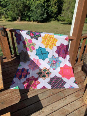 Woollypetals Floored quilt displayed on wooden deck with colorful star blocks