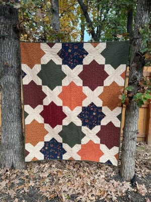 Woollypetals Floored quilt featuring star blocks in rust, navy, green, and burgundy