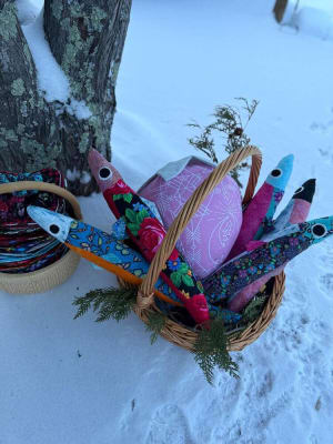 Woollypetals Sardine Pillow in colorful fabrics displayed in a wicker basket on snow