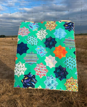 Woollypetals Floored quilt with colorful star blocks and black fabric displayed outdoors