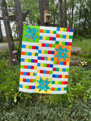 Woollypetals StarBeam quilt with colorful blocks and turquoise stars displayed outdoors