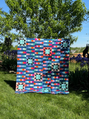 Woollypetals StarBeam quilt displayed on grass with colorful patchwork blocks