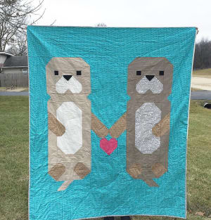 Woollypetals Don't Let Go Quilt featuring two otter figures on turquoise background