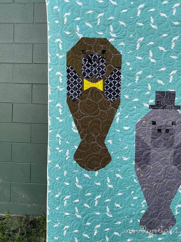Woollypetals Manatee Migration quilt block featuring brown manatee with yellow bow tie on turquoise background