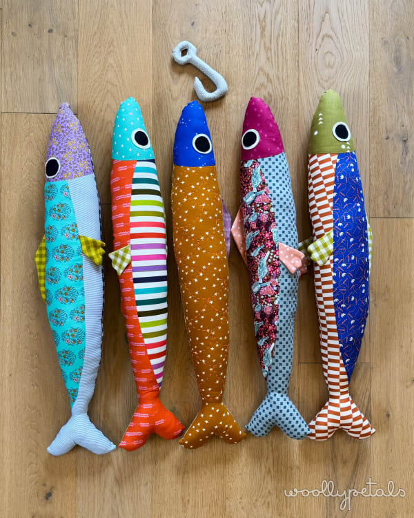 Woollypetals Sardine Pillow in five colorful fabric variations on wood floor