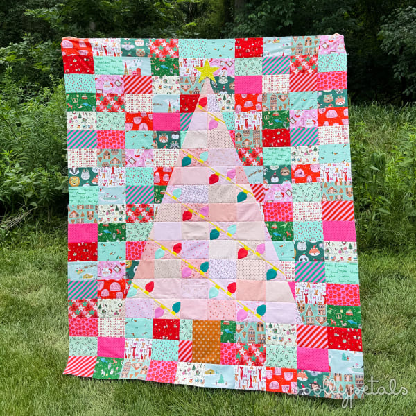 Woollypetals Oh Christmas Tree quilt displayed on grass with patchwork blocks and appliqué tree design