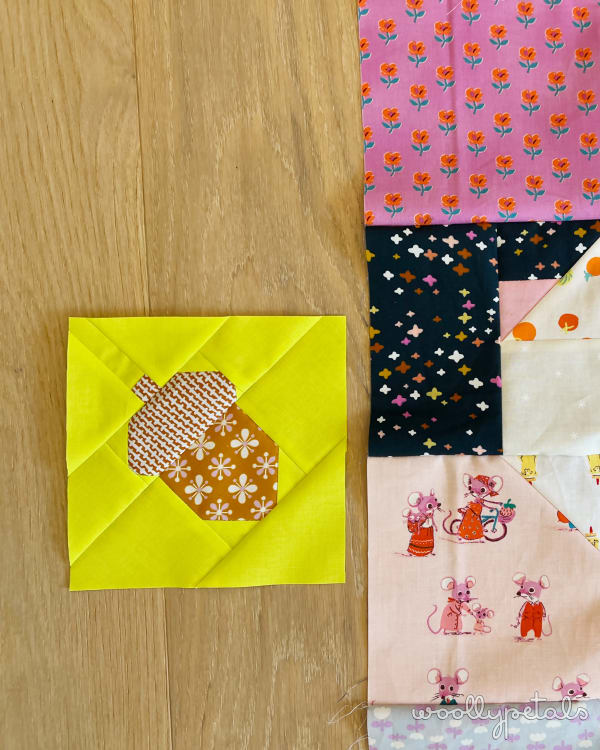 Woollypetals Squirrel quilt block with yellow background and patterned acorn appliqué