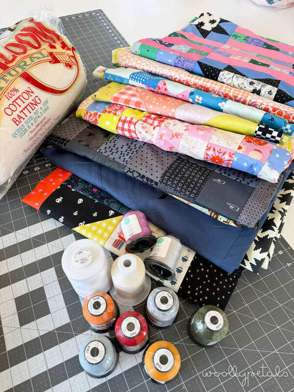 2 Week Quilt Top Challenge supplies including colorful fabric bundles, thread spools, and quilting tools on cutting mat