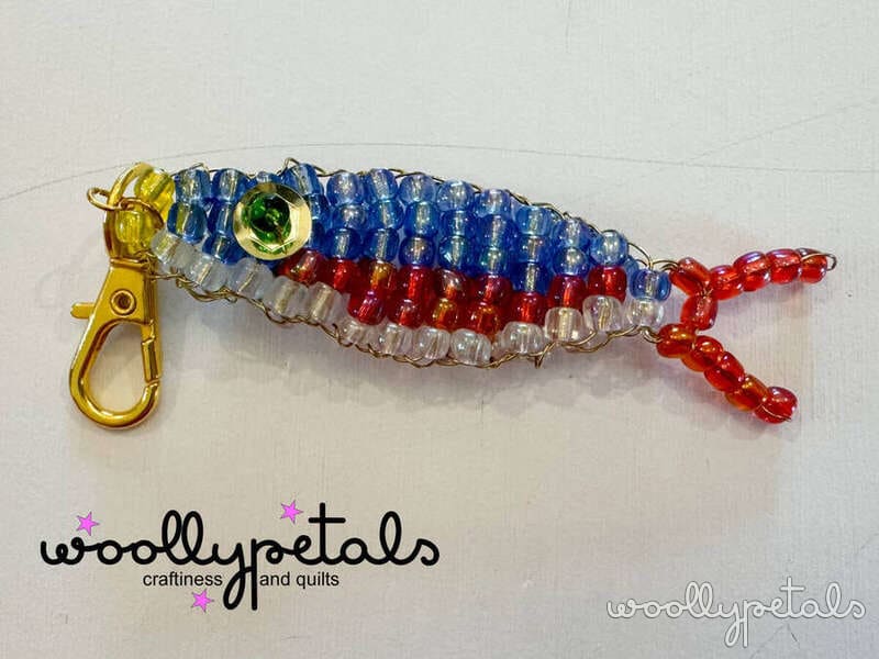 Woollypetals beaded sardine charm with blue, red, and clear beads on gold clasp