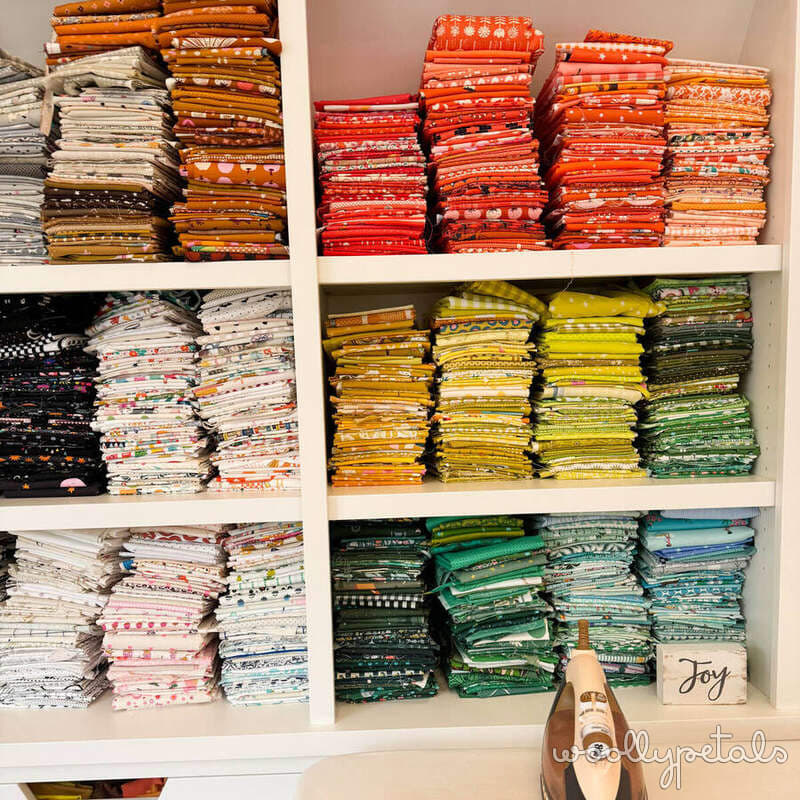 Organized fabric stash on white shelves sorted by color