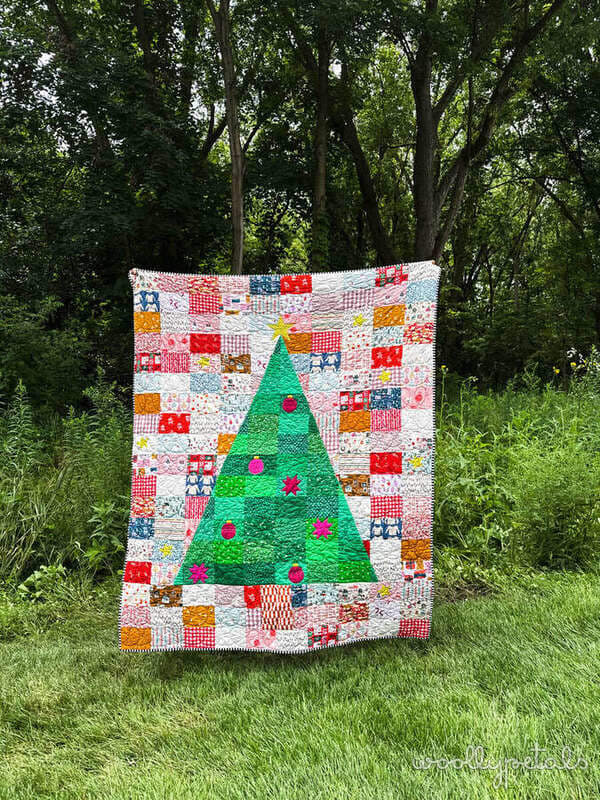 Christmas tree quilt with patchwork border and colorful ornaments hanging outdoors