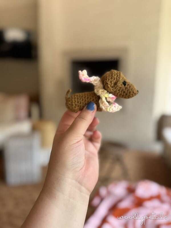 Crocheted brown dog with pink bow held in hand
