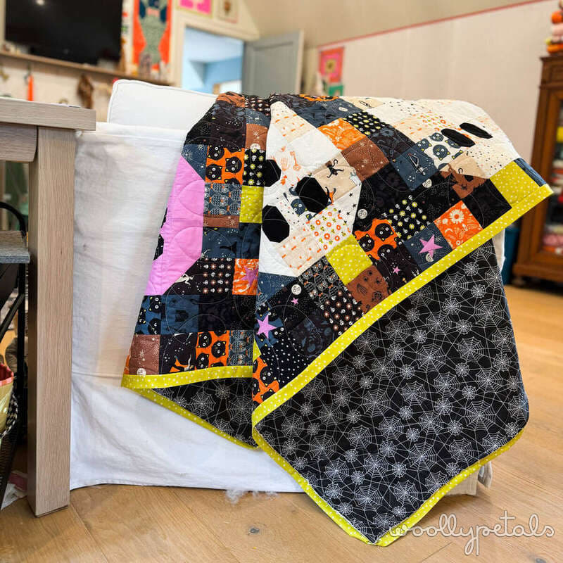Woollypetals Ghost Party quilt with Halloween fabric and yellow binding draped over chair