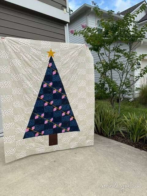 Woollypetals Oh Christmas Tree quilt displayed on garage wall with navy tree and pink ornaments