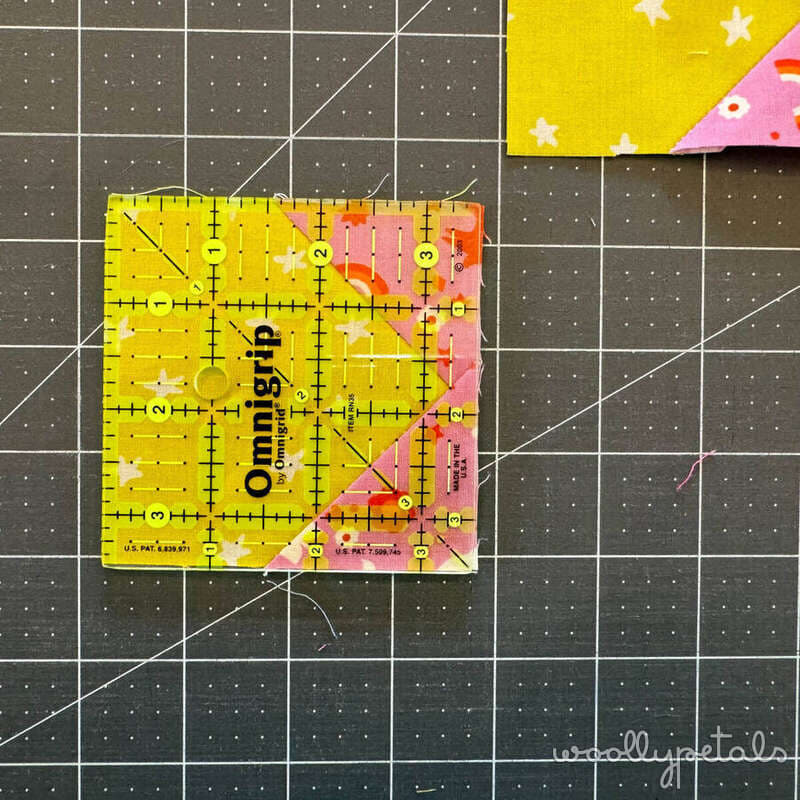 Woollypetals New Star quilt ruler placed on yellow and pink fabric squares on cutting mat