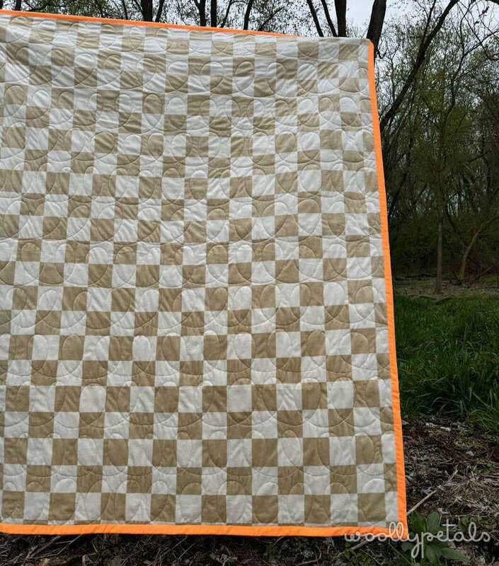 Woollypetals New Star beginner quilt with tan and cream checkerboard pattern backing displayed outdoors