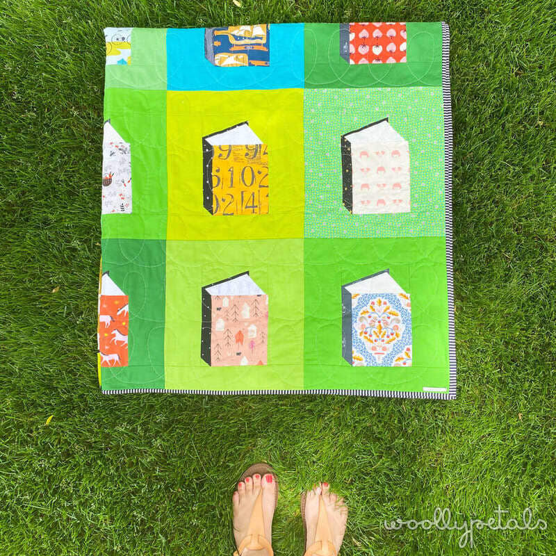 Woollypetals quilt with colorful fabric squares and book-shaped appliqués on grass