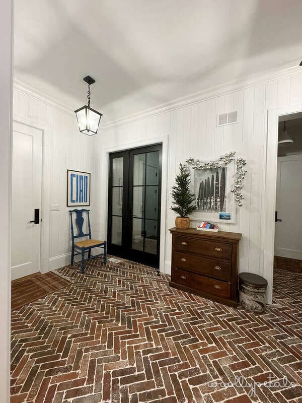 Modern entryway with herringbone brick flooring, white paneled walls, and black French doors