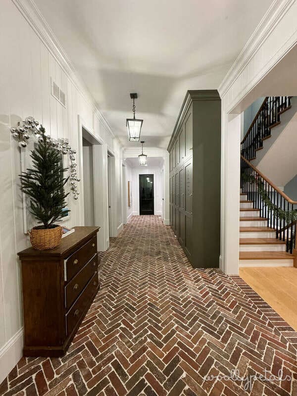 Elegant hallway with herringbone brick flooring, white paneling, and green cabinetry
