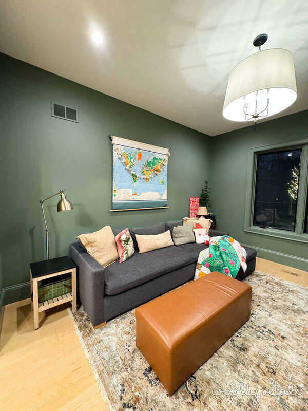 Green family room with gray sofa, leather ottoman, and world map