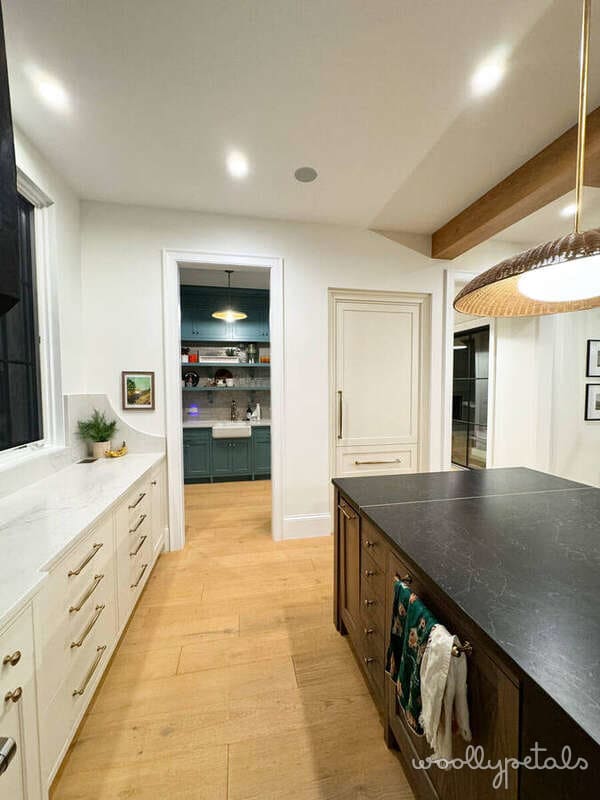 Modern kitchen with white cabinetry, dark island, and wooden beam ceiling