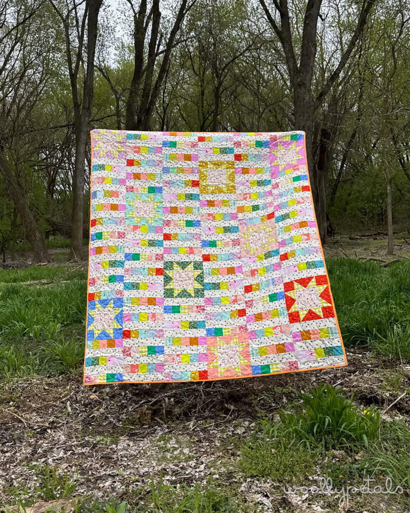 Woollypetals StarBeam Quilt displayed outdoors with colorful patchwork fabrics