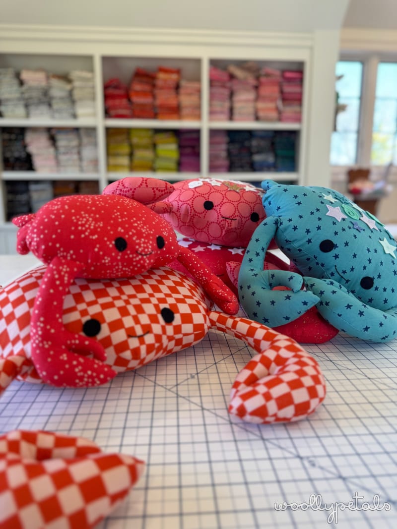 Woollypetals Coco the Crab stuffed animals in red, pink, and blue fabrics on crafting table